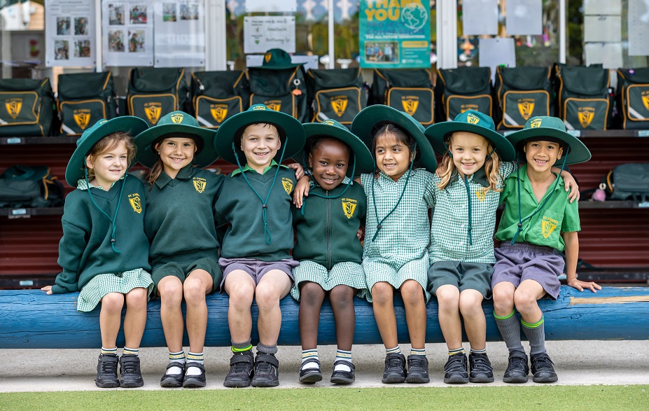 Students in school uniform sitting together on a bench at school.