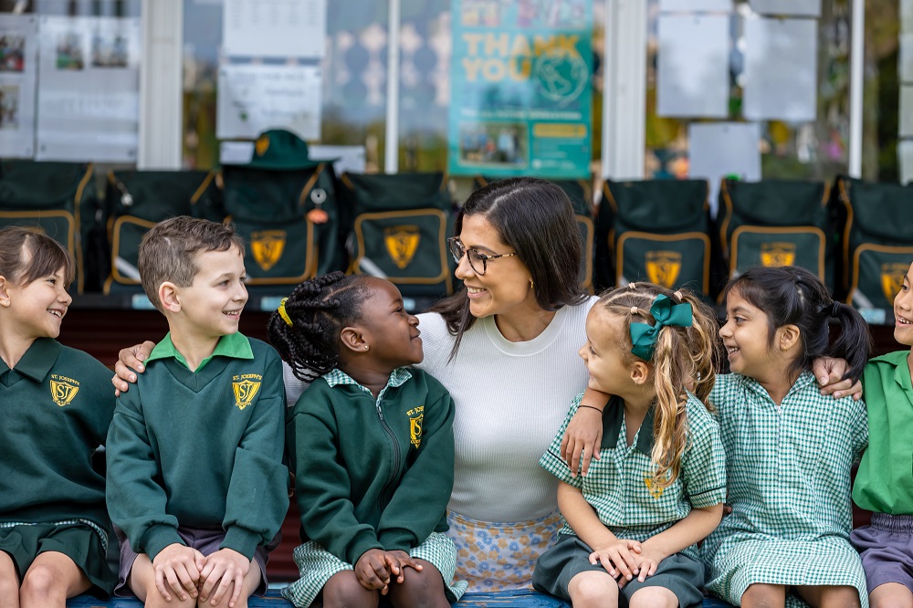 Adult sitting with students in school uniform on a bench at school.