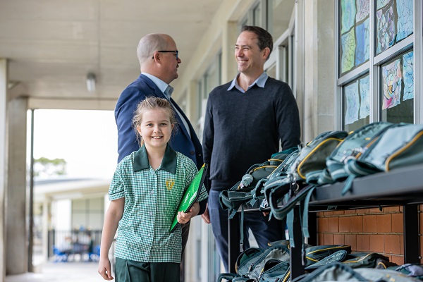Student walking along a school walkway with adults nearby and school bags on shelves.