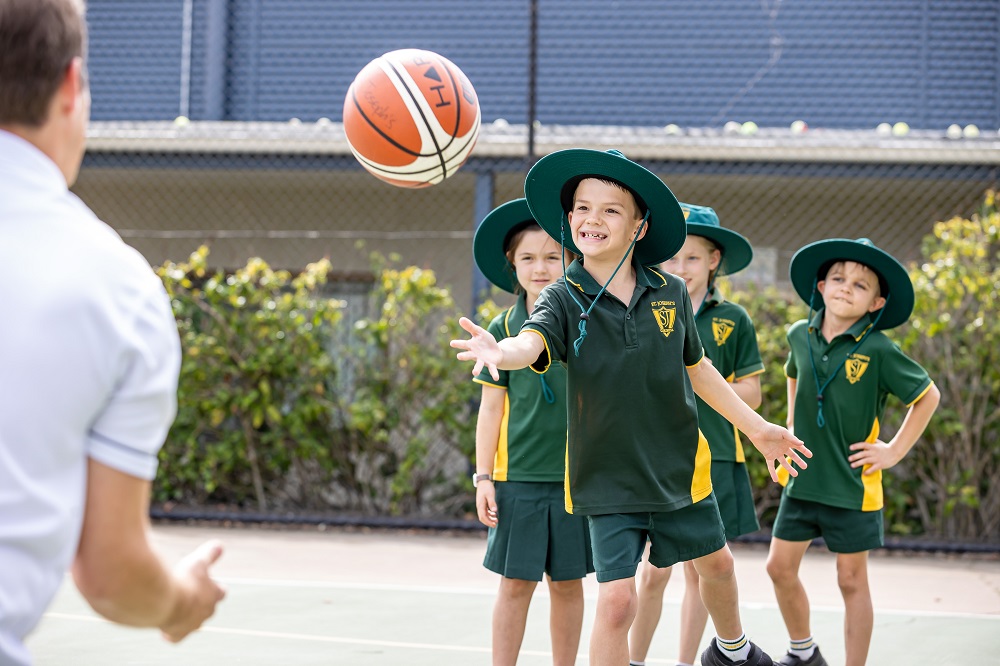 Students participating in a basketball activity during a physical education lesson on an outdoor court.