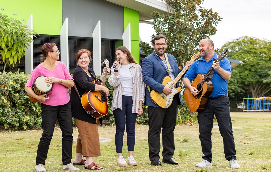Group of adults playing musical instruments together outdoors on school grounds.