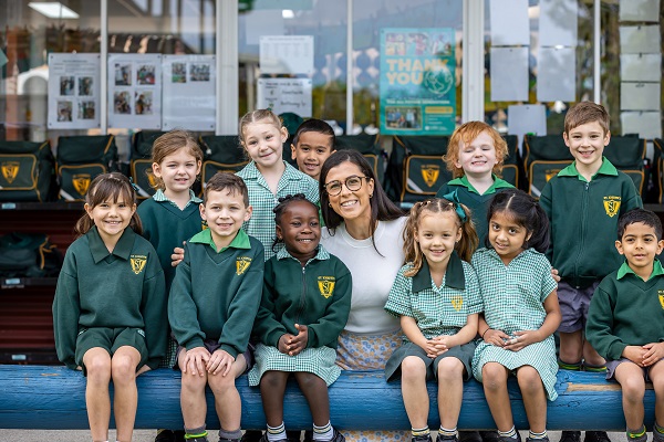 Adult sitting with students in school uniform on a bench at school.